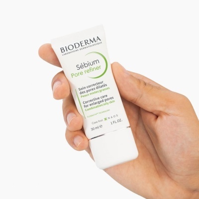 Mão segura tubo branco de produto Bioderma Sébium Pore Refiner com texto em francês e inglês