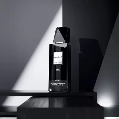 Frasco de perfume preto com rótulo branco em superfície escura com sombra na parede