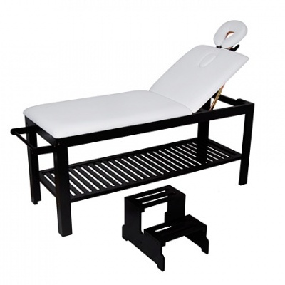 Cama de massagem com colchão branco e estrutura preta, com apoio de cabeça redondo e banco de apoio.
