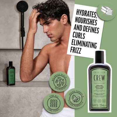 Frasco de shampoo American Crew e homem com cabelo encaracolado molhado numa casa de banho.