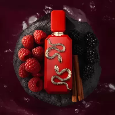 Frasco de perfume vermelho com serpentes prateadas ao lado de frutas e paus de canela