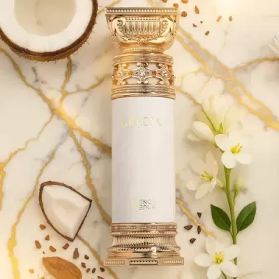 Frasco de perfume branco e dourado ornamentado sobre superfície marmoreada com meio coco, flores brancas e sementes.