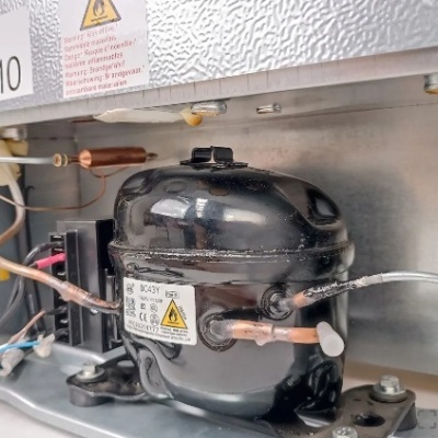 Compressore preto de frigorífico com tubos de cobre e etiqueta com aviso de risco