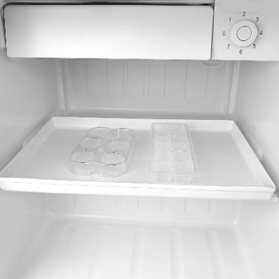 Interior de frigorífico branco com formas de gelo transparentes sobre prateleira