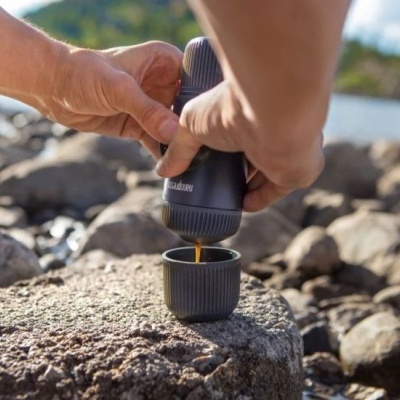 Pessoa a verter café de recipiente em copo pequeno sobre pedra ao ar livre