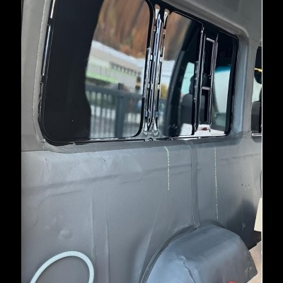 Interior de carrinha com paredes cinzentas, janela escurecida, tubo branco, caixa vermelha e preta e fita métrica no chão