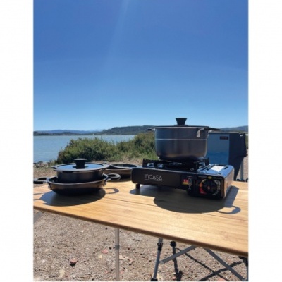 Fogão portátil com panela e frigideira sobre mesa de madeira ao ar livre.
