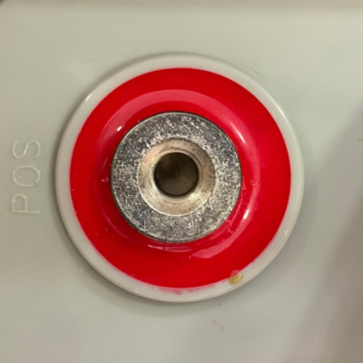 Conector elétrico vermelho e metálico em base cinza com texto POS