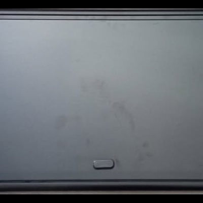 Tampa preta retangular com bordas arredondadas e três elementos retangulares em relevo.