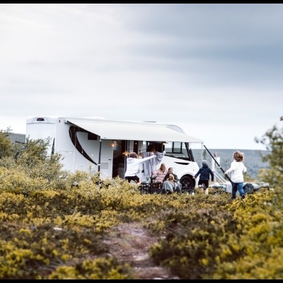 Autocaravana branca com família ao ar livre num local com vegetação