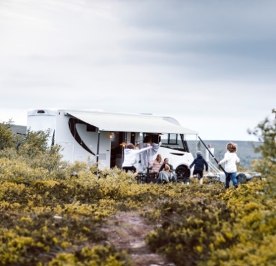 Autocaravana branca com família ao ar livre num local com vegetação