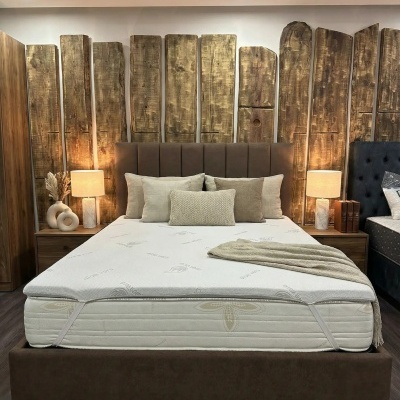 Cama de casal com colchão branco, estrutura castanha estofada, almofadas bege e cabeceira de madeira rústica vertical