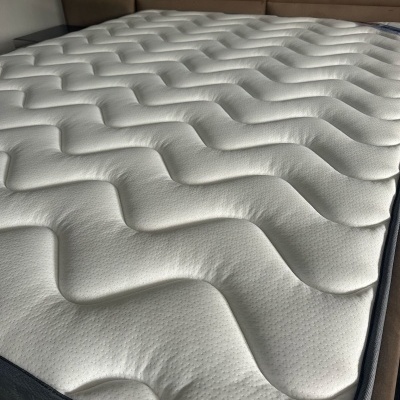 Colchão branco com padrão ondulado sobre cama com cabeceira castanha