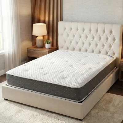 Cama estofada bege com colchão branco e cinza, mesa de cabeceira de madeira com candeeiro e planta