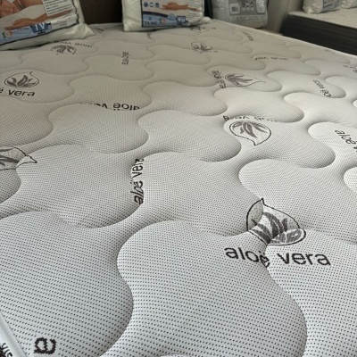 Colchão cinza claro com padrão acolchoado e texto aloe vera com folhas, almofadas viscoelásticas embaladas ao fundo