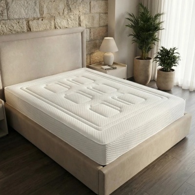 Colchão branco em cama estofada bege numa sala com planta e lâmpada