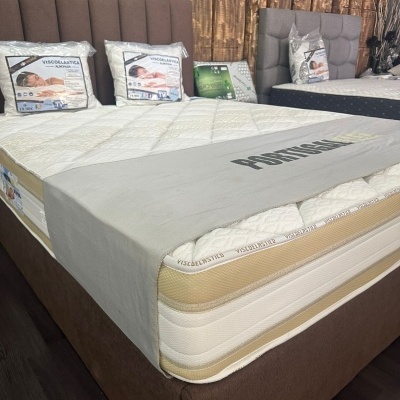 Cama com colchão viscoelástico branco e bege com capa cinzenta com palavra PORTUGAL e cabeceira castanha