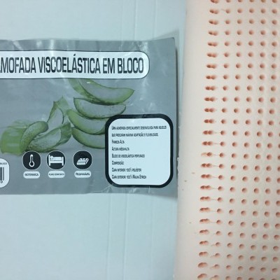 Almofada viscoelástica creme perfurada ao lado da embalagem cinzenta com etiqueta