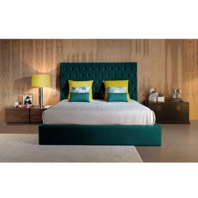 Cama estofada verde escura com cabeceira almofadada, almofadas amarelas e verdes, mesas de cabeceira de madeira e candeeiro