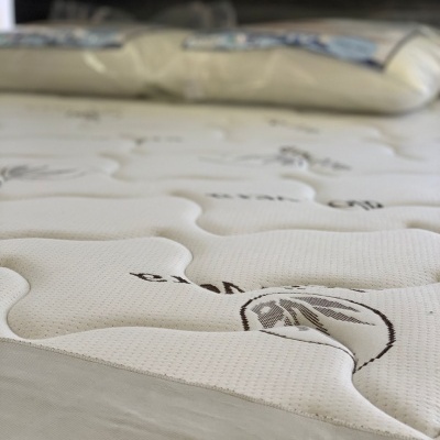 Colchão branco acolchoado com bordas cinza e texto parcial, em ambiente interno.