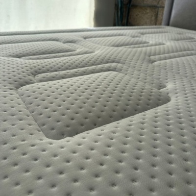 Colchão branco texturizado em cama cinzenta com parede de pedra ao fundo