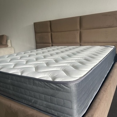 Colchão branco e cinza numa cama estofada castanha com cabeceira almofadada