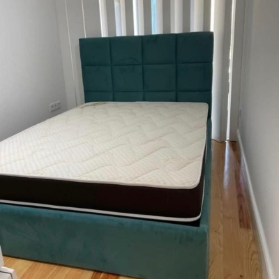 Cama verde estofada com colchão branco numa divisão com chão de madeira