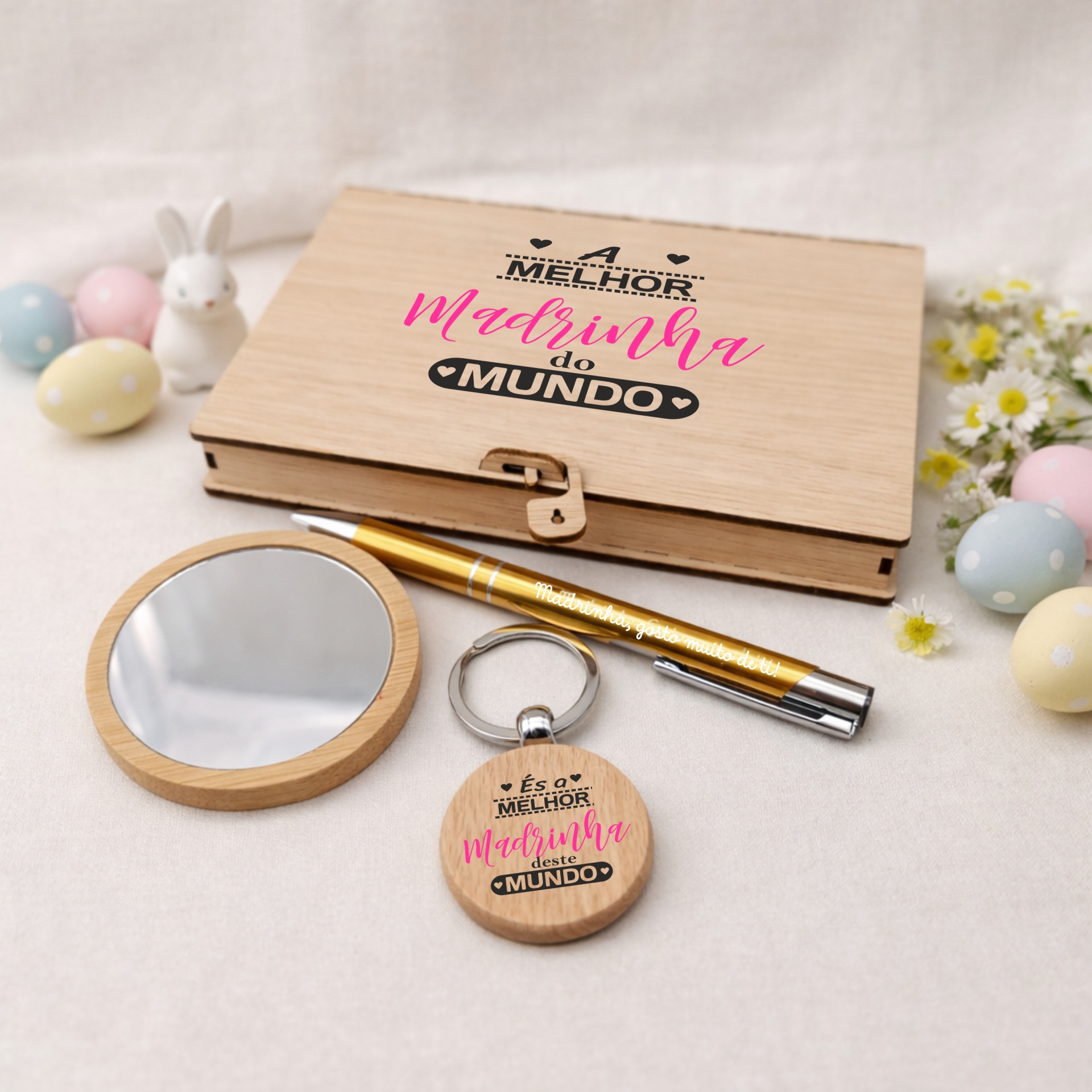 Caixa 'Melhor Madrinha do Mundo' - Personalizada Conjunto de presente para madrinha com caixa de madeira, espelho, caneta dourada e porta-chaves, decorado com ovos e coelho, em fundo neutro.