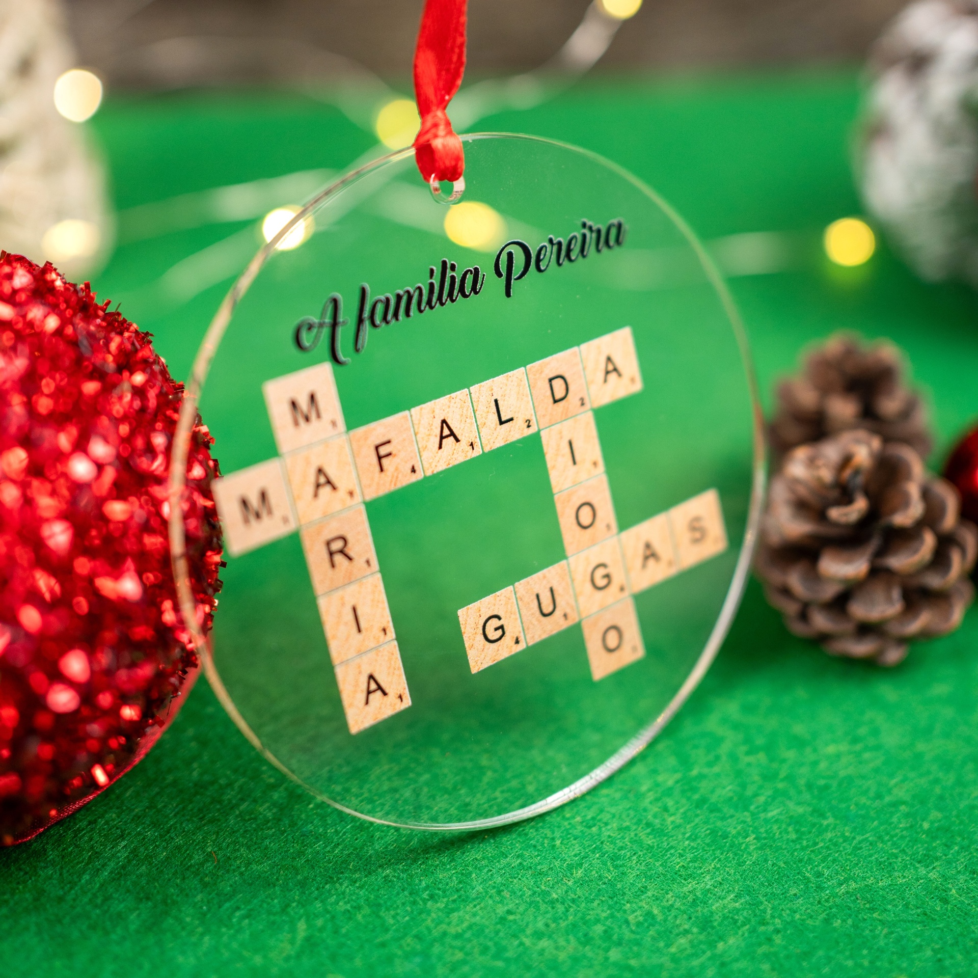 Bola de Natal Scrabble Personalizada com Nomes Ornamento Natalício redondo transparente com fita vermelha com letras de madeira e texto A família Pereira.