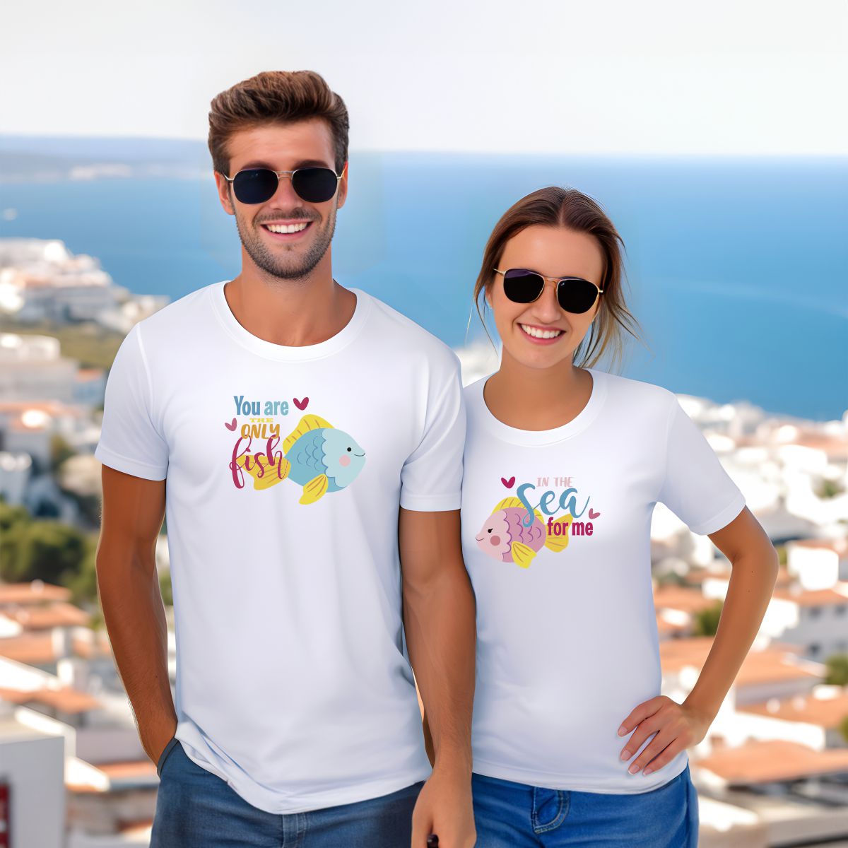 Homem e mulher a usar t-shirts brancas com desenhos de peixes e frases em inglês, em fundo de mar e casas brancas.