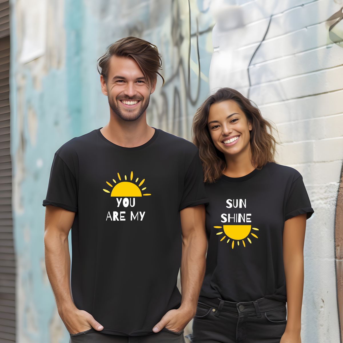 Casal com t-shirts pretas estampadas com meio sol amarelo e texto branco posando ao ar livre