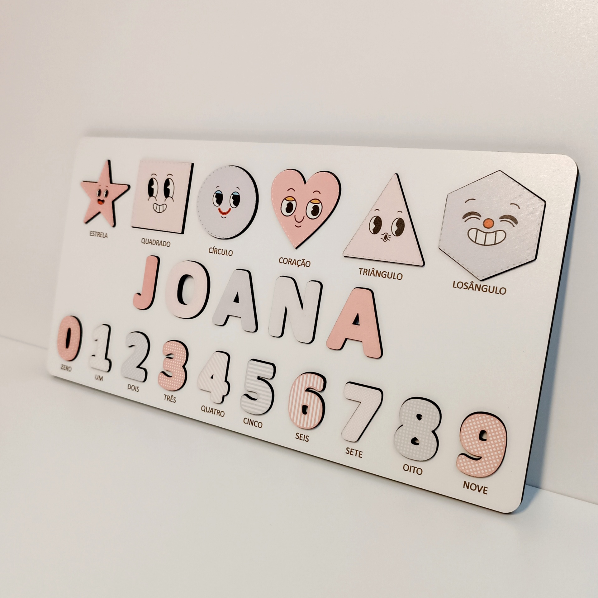 Jogo de Encaixe Personalizado – Formas, Números e Nome (rosa) Quadro branco com peças em madeira e formas geométricas e números sorridentes em tons rosa e branco.