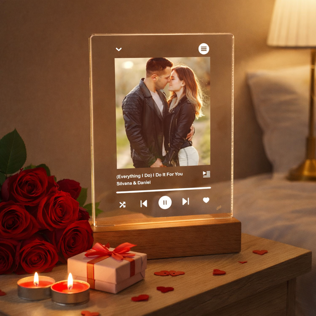 Candeeiro LED Personalizado Fotografia - Modelo "Música Namorados" Luminária de madeira e acrílico com foto de casal e texto de música, com velas acesas, rosas e presente numa mesa ao lado da cama.