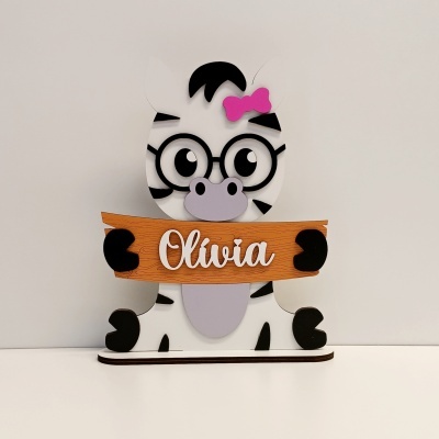Figura decorativa de zebra com laço rosa e placa de madeira com nome Olívia.
