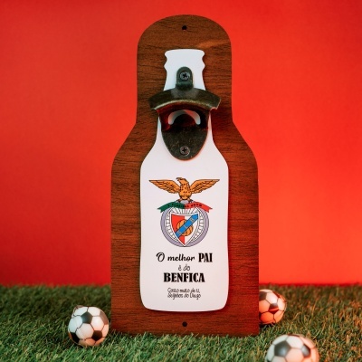 Abridor de garrafas em madeira com brasão e texto sobre fundo vermelho e relva com bolas de futebol pequenas