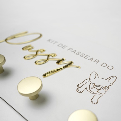Puxadores de mobília dourados redondos numa placa branca com texto e desenho de buldogue