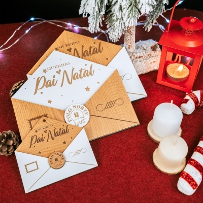 Cartões de Natal em madeira e papel com selo Polo Norte, velas, pinhas e decoração natalícia sobre superfície vermelha