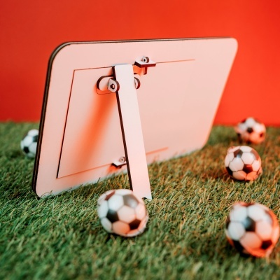 parte traseira de quadro ou ecrã branco com suporte, bola de futebol ao fundo, relva e fundo vermelho