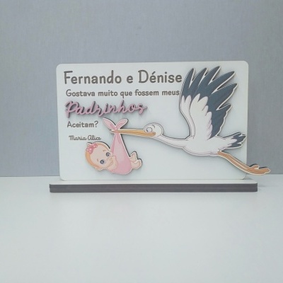 Placa de madeira com texto em português e ilustração de cegonha com bebé