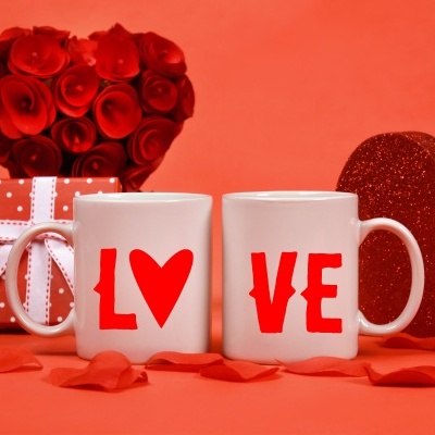 Duas canecas brancas com a palavra LOVE em vermelho e objetos decorativos em tons de vermelho