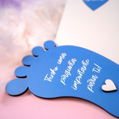 Placa decorativa azul em forma de pé com texto em português e um coração branco sobre fundo rosa.