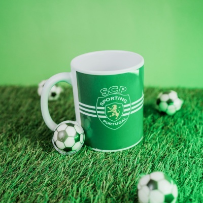 Caneca verde do Sporting Portugal com bolas de futebol sobre relva artificial.