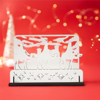 Escultura dos três reis magos em metal branco com base preta e fundo vermelho com luzes