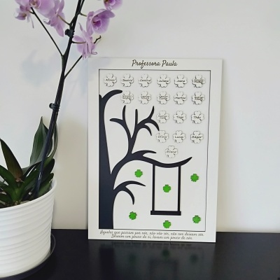 Quadro branco decorativo com árvore, flores e nomes, planta verde em vaso branco ao lado