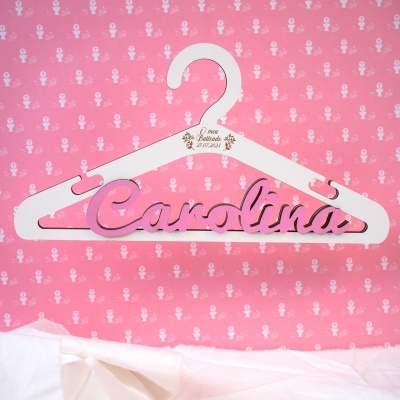 cabide branco com nome Carolina em rosa e texto O meu Batizado 27.07.2024, fundo cor-de-rosa com padrão religioso