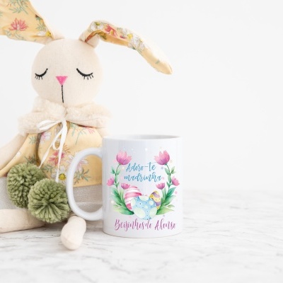 Caneca branca decorada com texto e flores junto a coelho de pano com orelhas floridas