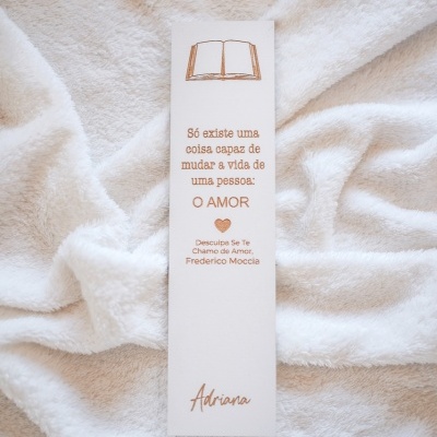 Marcador de livros branco com texto sobre amor e nome Adriana sobre tecido branco felpudo