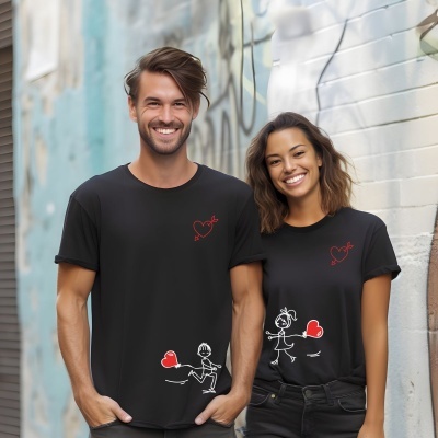Homem e mulher com t-shirts pretas com desenhos de corações e figuras estilizadas, posando ao ar livre numa rua com parede grafitada.
