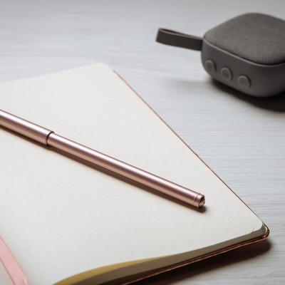 Caderno aberto com caneta metálica e coluna portátil cinzenta ao fundo