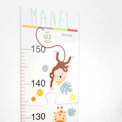 Medidor de crescimento infantil com desenhos de macaco e girafa, e texto informativo, montado na parede branca.